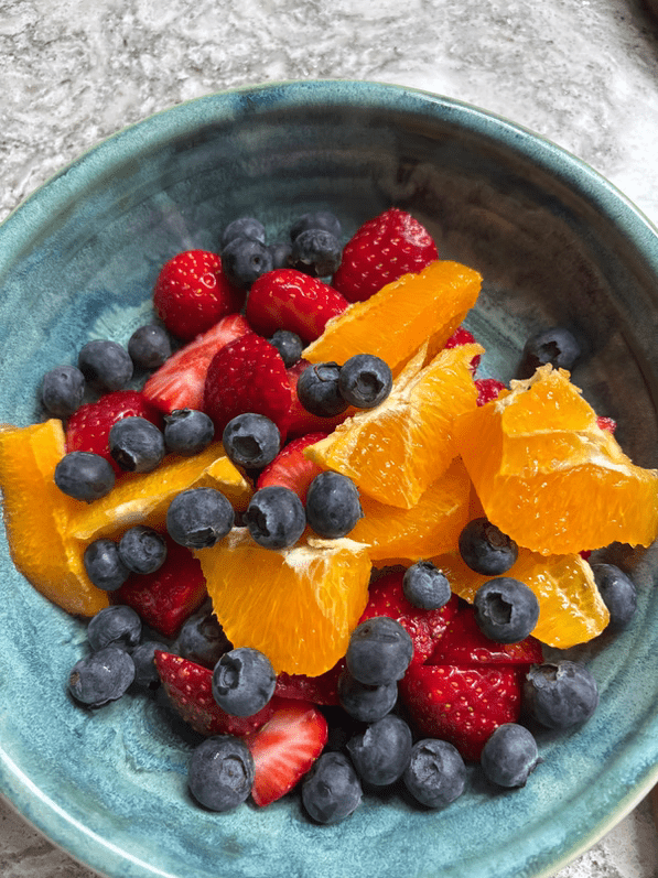 Colorful bowl of mixed fruit featuring strawberries, blueberries, and orange slices, showcasing a fresh and healthy snack option.